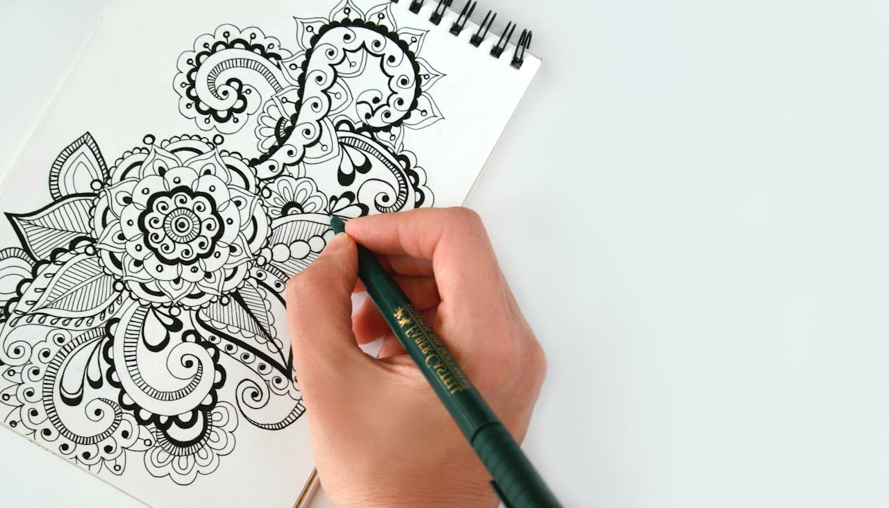 Close-up of a hand drawing an intricate mandala pattern on a sketchbook using a pen. Perfect for creativity themes.